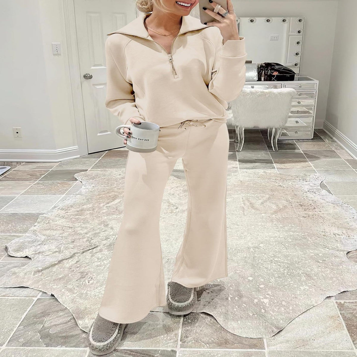 Woman in a cream half-zip sweatshirt and wide leg pants set holding a mug